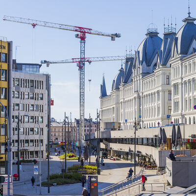 Bygate med bygninger, fotgjengere og flere byggekraner i bakgrunnen.