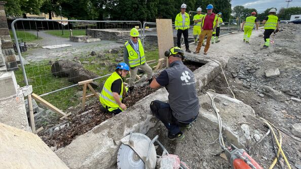Flere arbeidsfolk ser på ruiner i stein.
