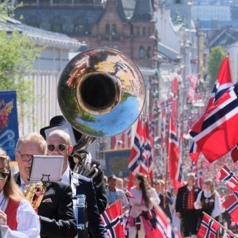 Et korps som spiller og mange mennesker som flagger med norske flagg i Karl Johan.