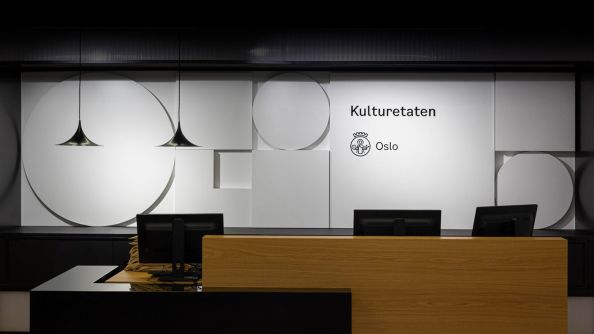 Resepsjon Kulturetaten, med moderne resepsjonspult i forgrunnen og Osloformer i hvitt på veggen bak.
