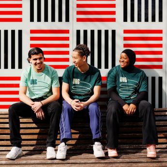 Tre ungdommer sitter på en benk og smiler. Alle har på seg lik t-skjorte det står "Ung" på.