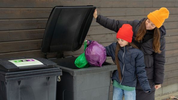 Dame og jente som kaster en grønn og en lilla søppelpose.