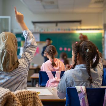 Barn som rekker opp hendene i et klasserom.