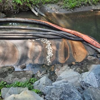 Oljeutslipp i en elv, med sorte og oransje ledninger som skiller forurenset vann fra rent vann