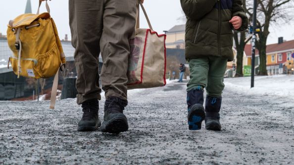 Nærbilde av bena til far og sønn som går på is og grus ved Jordal idrettsplass.