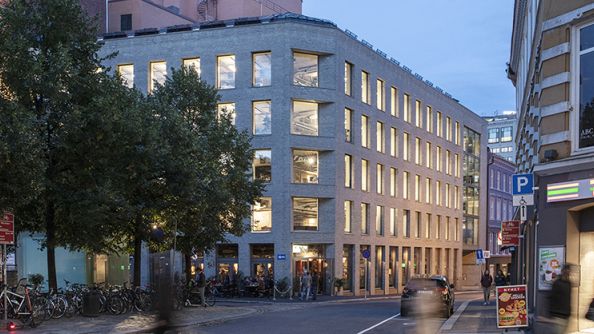 Grått murbygg på fem etasjer, med lys fra alle vinduene. Serveringssted i første etasje.