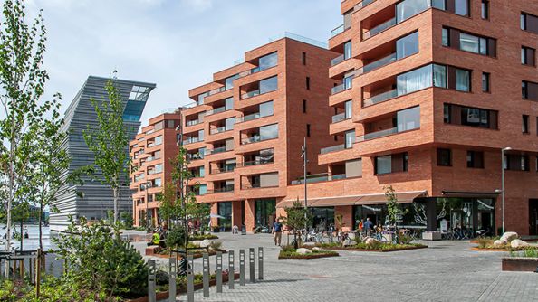 Oransje teglesteinblokker med store vindusflater og verandaer. Munchmuseet i bakgrunnen.
