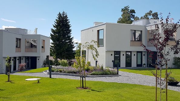 To hvite boligbygg med flatt tak på et tun.