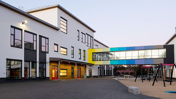 To hvite skolebygg med en fargerik lukket bru mellom