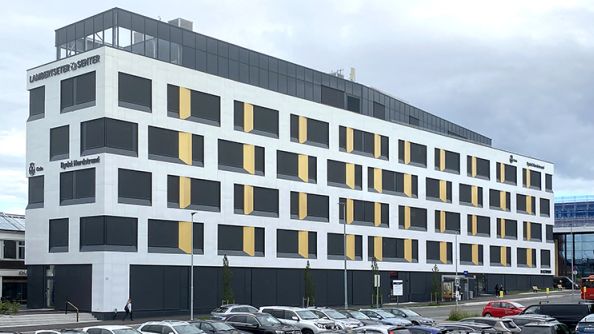 Seksetasjes hvitt kontorbygg, hvor den øverste etasjen er litt lenger inn enn de andre.