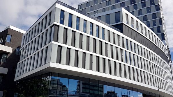 Bilde av stort hvitt kontorbygg, tatt i froskeperspektiv. Glassfasade i første etasje.