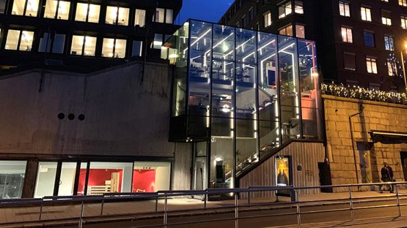 Firkantet glassbygg mellom steinmur og murbygg.