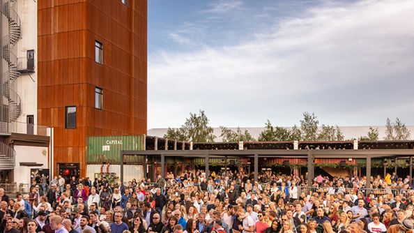 Sittende folkemengde, høyt bygg i bakgrunnen.