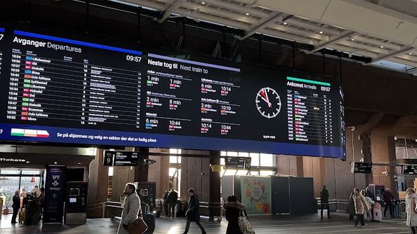 A photo of the sun streaming through the train station while people walk beneath the arrival and departure signs