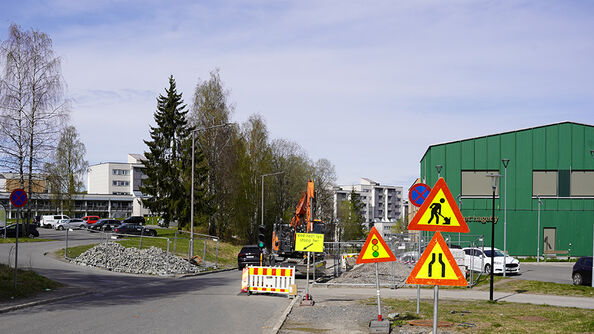Kryss med veiarbeid, sperringer og varselskilt, og gravemaskin bak avsperring.