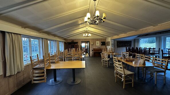Spisesal med bord, stoler og store vinduer.