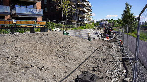 Anleggsområde med gravemaskin og arbeidere ved boligblokker.