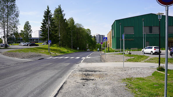 Kryss med gangfelt ved vei, omgitt av trær og bygninger.