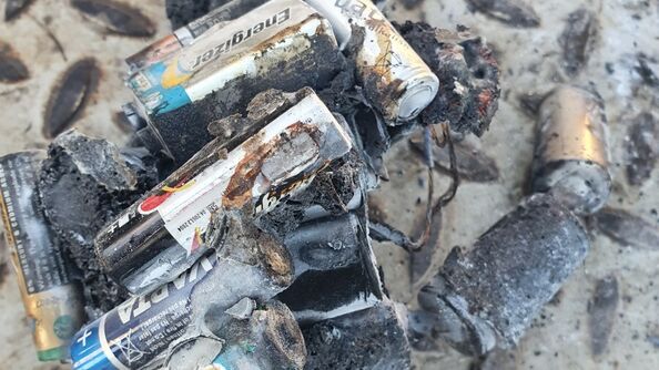 Nærbilde av brukte batterier som er brannskadet og delvis smeltet etter en brann. Batteriene ligger blant aske og forkullet materiale og illustrerer risikoen ved å kaste batterier i restavfallet.