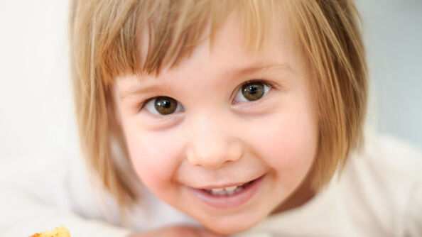 Liten søt, troskyldig, blid jente ser rett i kamera.