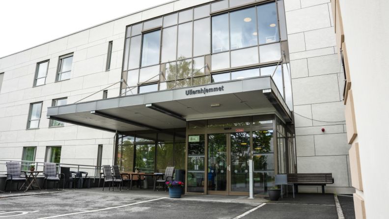 Fasaden og inngangspartiet til Ullernhjemmet. Over inngangsdøren er det et tak og rundt finnes det benker og stoler. 