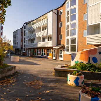 Blokk på Åsbråten med benker og trær rundt