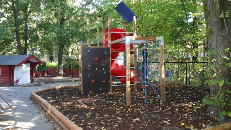 Uteområde med klatrestativ med sklie sett bakfra, sandkasse bakgrunnen, med trær rundt