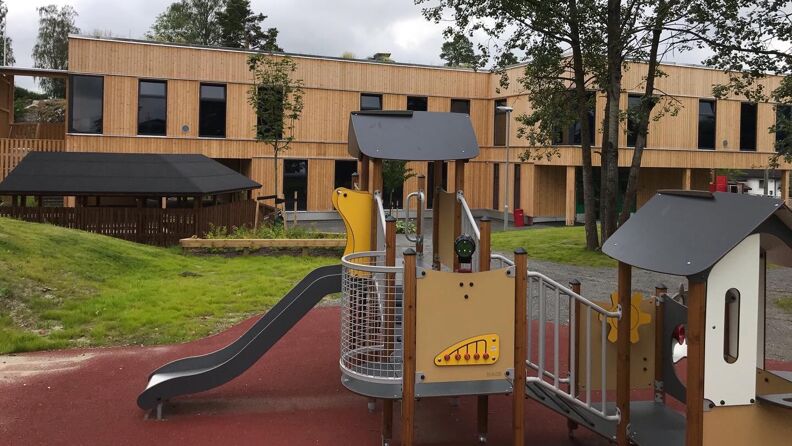 Klatrestativ med sklie, i bakgrunnen er barnehagen med lys fasade i tre
