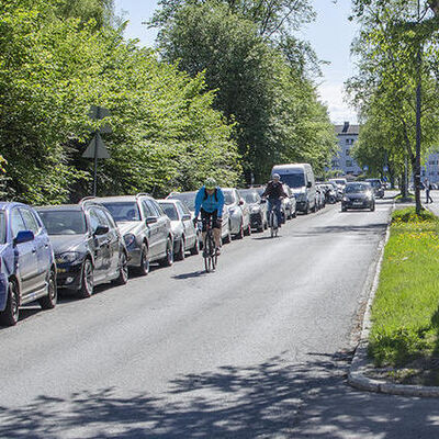 To syklister på en gate med parkerte biler langs veien.