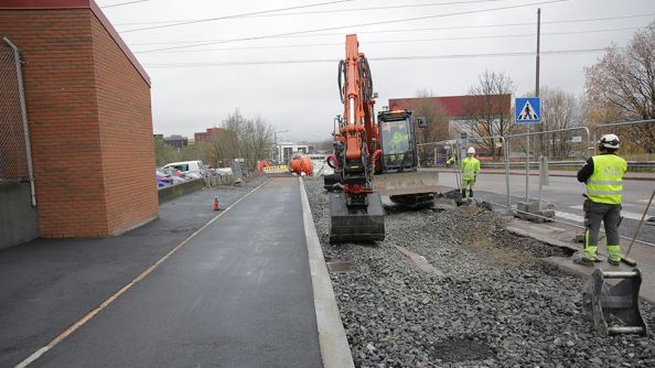 En gravemaskin og to arbeider som jobber med å byge holdeplass og sykkelvei.